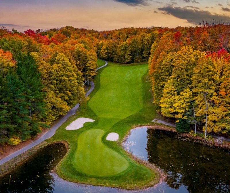 A golf hole framed by brilliant autumn foliage and water